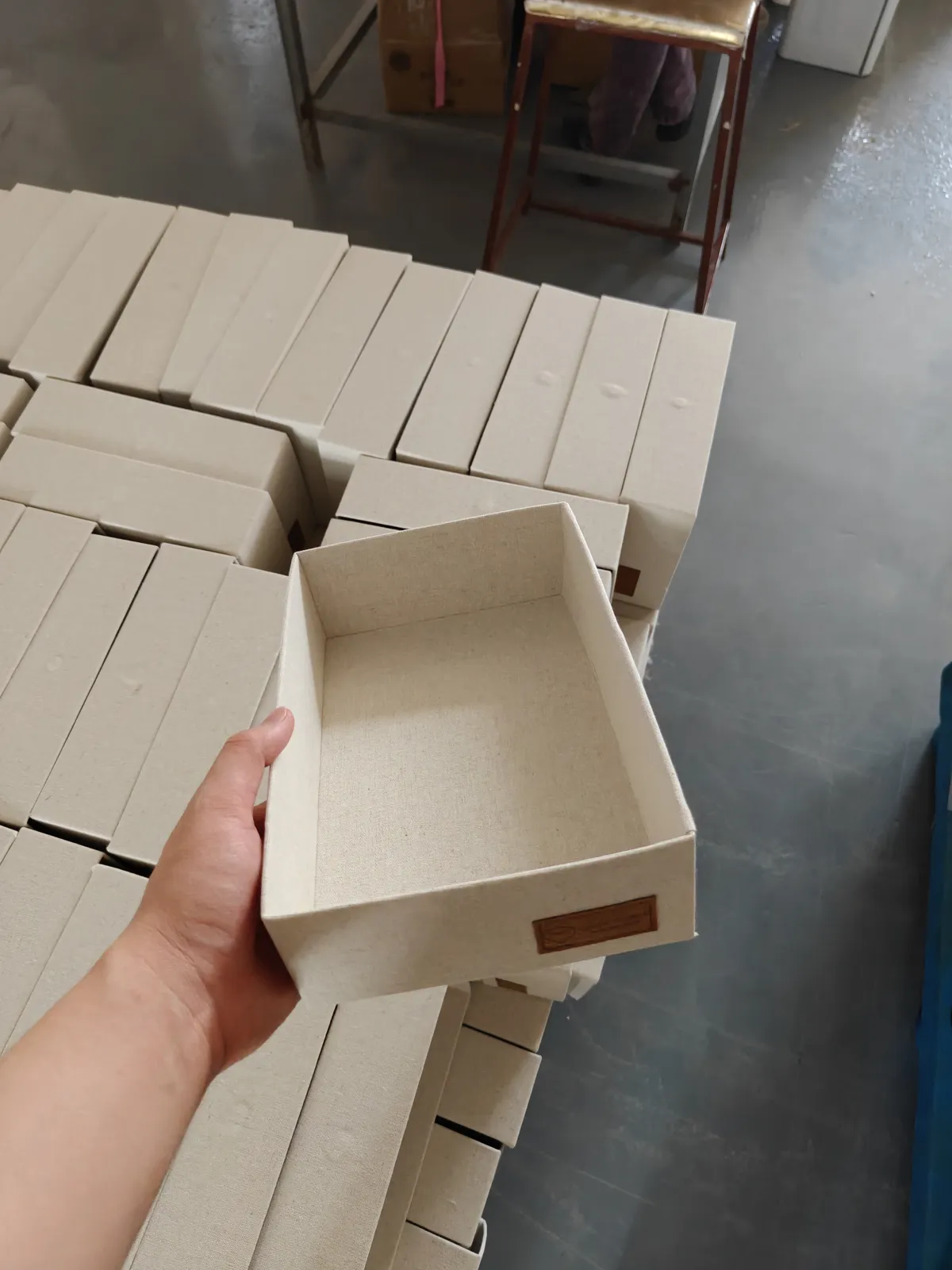 Natural linen storage tray with leather logo patch, held in hand at the factory